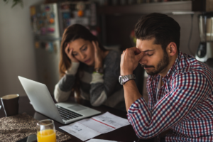 Debt: It could happen to anyone. Man and woman sitting in front of laptop with bill on the table and their heads in their hands looking concerned
